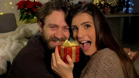 Couple in love looking camera smiling in front of christmas tree with gift do Stock Footage 79622744