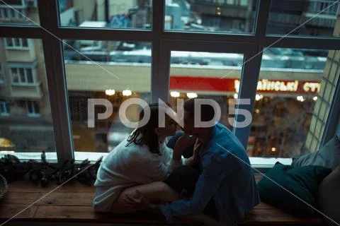 Couple in love sit in a hug on windowsill against the background of lights of Stock Photos