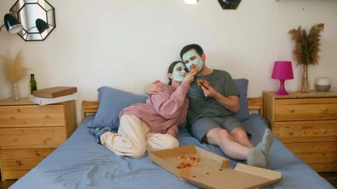 The couple is lying on the bed and feeding each other pizza Stock Footage 244369710