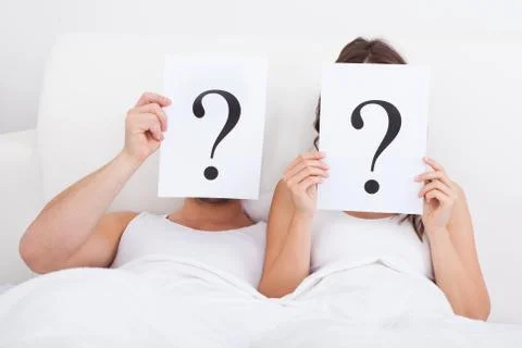 Couple lying on bed holding question mark on face Stock Photos