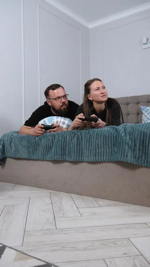 Couple lying on bed playing videogames together Stock Footage 317444687