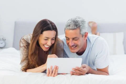 Couple lying on bed using their tablet pc Foto stock