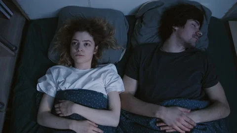 A couple is lying in bed, a young man is sleeping,and a young woman cannot sleep Stockbeeldmateriaal 197363963