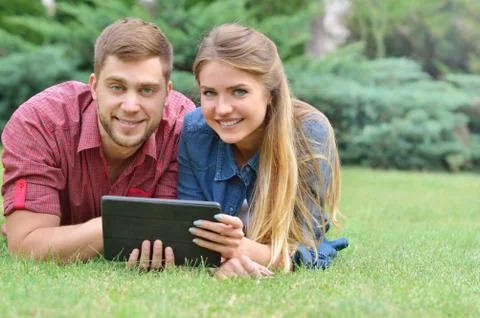 Couple lying in park using tablet pc together on a sunny day Stock Photos