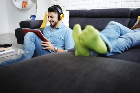 Couple Lying On Sofa With Tablet PC and Earphones Stock Photos