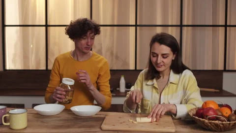 Couple making breakfast in a modern kitchen, cutting bananas, preparing cereal Stock Footage 278341202
