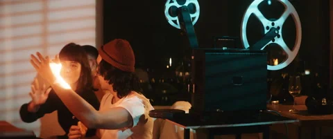 Couple making hand gestures in light of a vintage projector Stock Footage 202265768