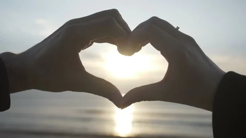Couple making heart shape with their hands with sunset inside on the beach in Stock Footage 90607164