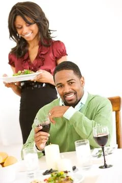 Couple: man looking to camera while girlfriend brings dinner Stock Photos