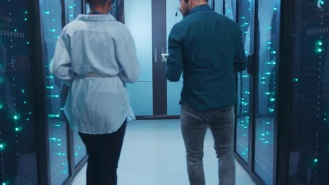 Couple of mixed-race technicians walking in database corridor of server room Stock Footage 119842858