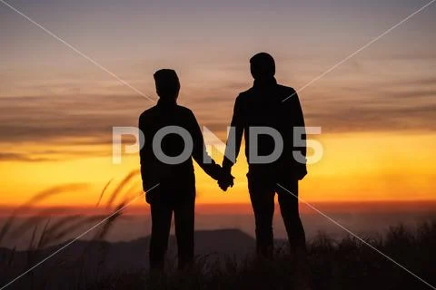The couple on the mountain enjoying a picturesque sunset background Stock Photos