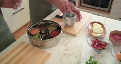 Couple in olive aprons pointing at spice tin on counter, grinding paste in Stock Footage 344851277
