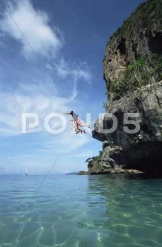 Couple outdoors jumping off cliff into ocean Stock Photos