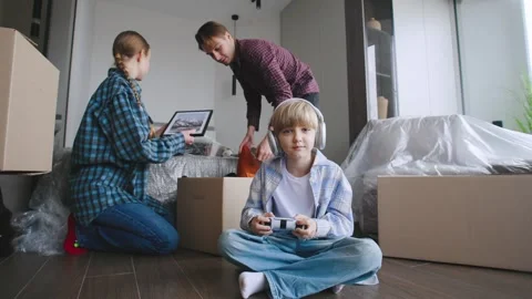 The couple is packing things while their son sits on the floor playing a video Stock Footage 346225591