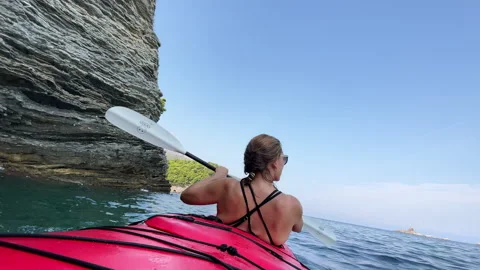 Couple paddling red two-seated kayak along the vertical layered cliff coast by c Stock-Footage 304975588