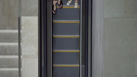 A couple passes by riding an escalator from a direct birds eye aerial view Stock Footage