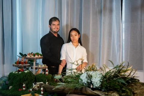 A couple of people stand at a set table with snacks, dishes and decorations Фото
