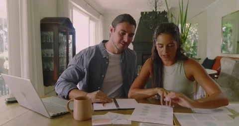 Couple placing chart at table, spreading printouts, tapping laptop, comparing Stock Footage 316667940