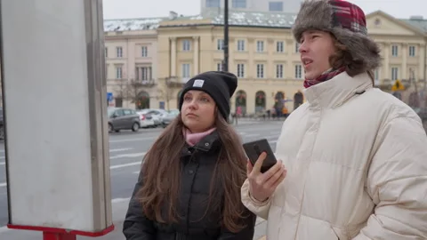 Couple planning a trip by checking a transport schedule at a city bus stop Stock Footage 311461498