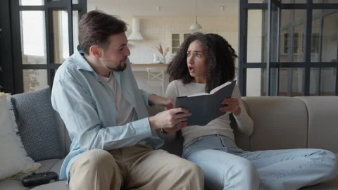 Couple Playfully Competing To Read The Same Book On Couch At Home Видео 306699716