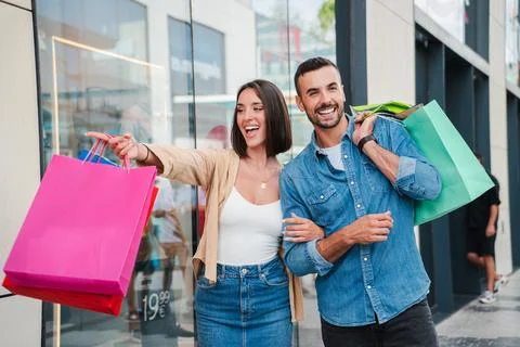 A couple points at the display of a store in the mall, deciding whether to buy Stock Photos