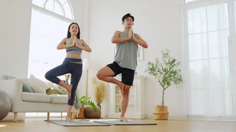 Couple practicing yoga in a bright, modern living room during morning hours for Stock Footage 300021300