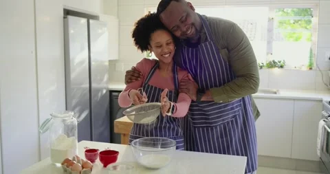 Couple preheating oven, sifting flour, cracking egg and stirring batter on Stock Footage 320146932
