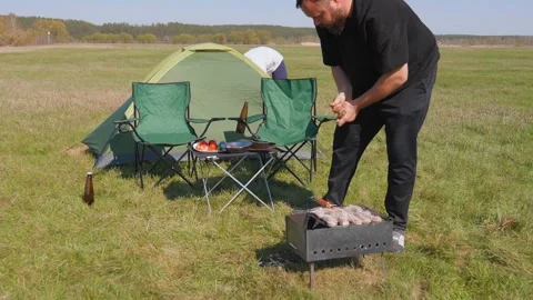 Couple preparing a barbecue on a sunny day during a camping trip Stockbeeldmateriaal 344606286
