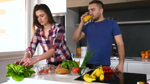 Couple preparing saland in the kitchen. Man is drinking juice Stock Footage 61859496