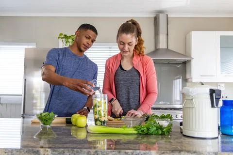 Couple preparing smoothie in modern kitchen, man pouring into blender jar, woman Stock Photos