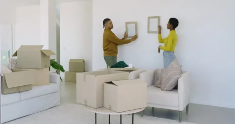 Couple pulling frames from boxes and decorating wall in home, hugging and Stock Footage 313227950