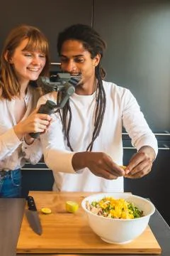 Couple putting lemon to a salad while they record it with the mobile Stock Photos