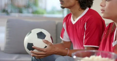 Couple reacting to off-screen match by rotating soccer ball on sofa at home Video stock 336715508