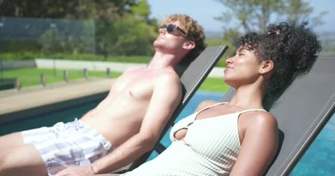 Couple reclining chairs poolside man shifting, raising shades, smiling, greeting Stock Footage 337400356