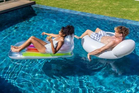 Couple reclining on pool floats in backyard pool, woman holding stemless glass Foto stock