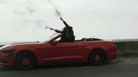 Couple in red cabriolet keep checkers in their hands with coloured smoke Stock Footage 172254714