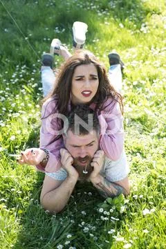 Couple relax on green grass. Woman smoke cigarette lying on man with daisy in Stock Photos