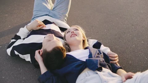 Couple relaxes on asphalt surface during sunset, enjoying intimate moment filled Stock Footage 314405271