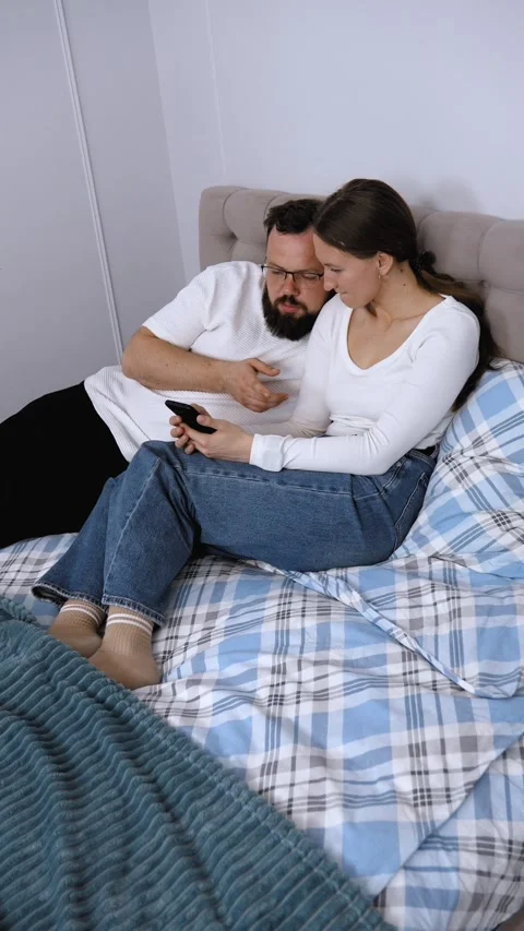 Couple relaxing in bed browsing smartphone together Stock Footage 320500354