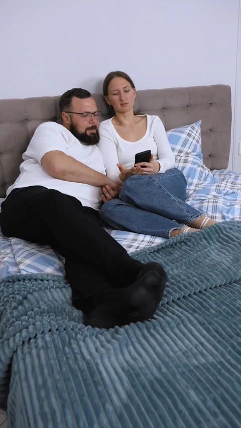 Couple relaxing in bed browsing smartphone together Stock Footage 320500426