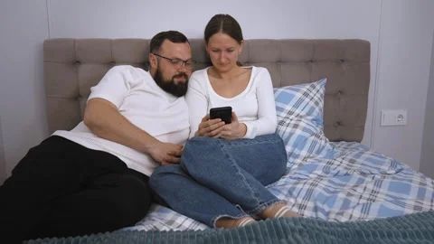 Couple relaxing on bed browsing smartphone together Stock Footage 320500448
