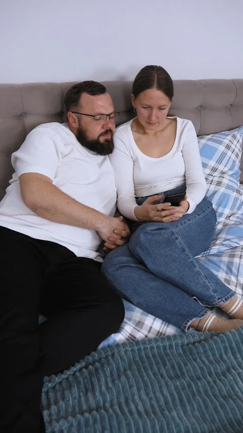 Couple relaxing on bed browsing smartphone together Stock Footage 320500450