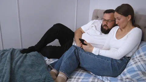 Couple relaxing on bed browsing smartphone together Stock Footage 320500463