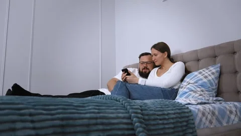 Couple relaxing on bed browsing smartphone together Video stock 320501613