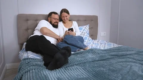 Couple relaxing on bed browsing smartphone together Video stock 320501629