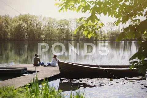 Couple relaxing on dock at sunny lakeside near canoe Stock Photos
