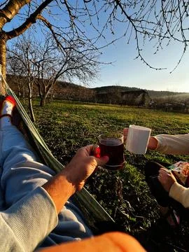 Couple relaxing in a hammock sharing tea and coffee in a sunny orchard at g.. Stock Photos