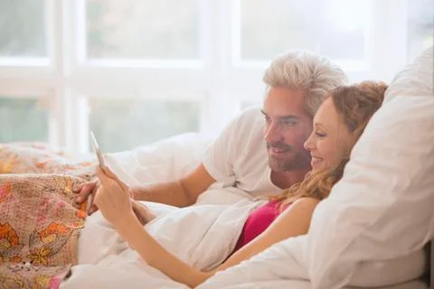 Couple relaxing laying in bed using digital tablet Stock Photos