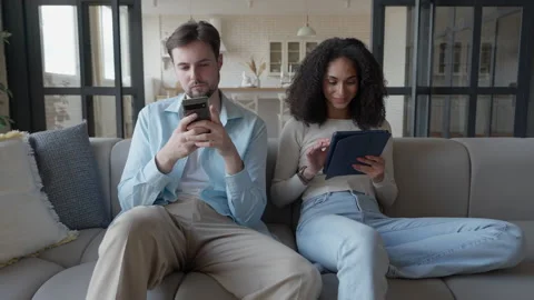 Couple Relaxing On Sofa Focused On Their Devices, Browsing Smartphone And Tablet Stock Footage 303759193