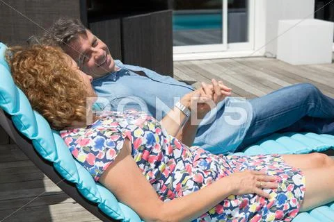 Couple relaxing on a sun lounger near pool Stock Photos